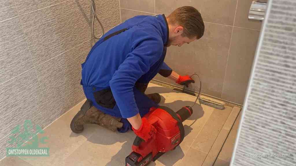 Een monteur ontstopt een langwerpige douchegoot met een elektrische veer, een doucheputje verstopt door haren en zeep in Oldenzaal