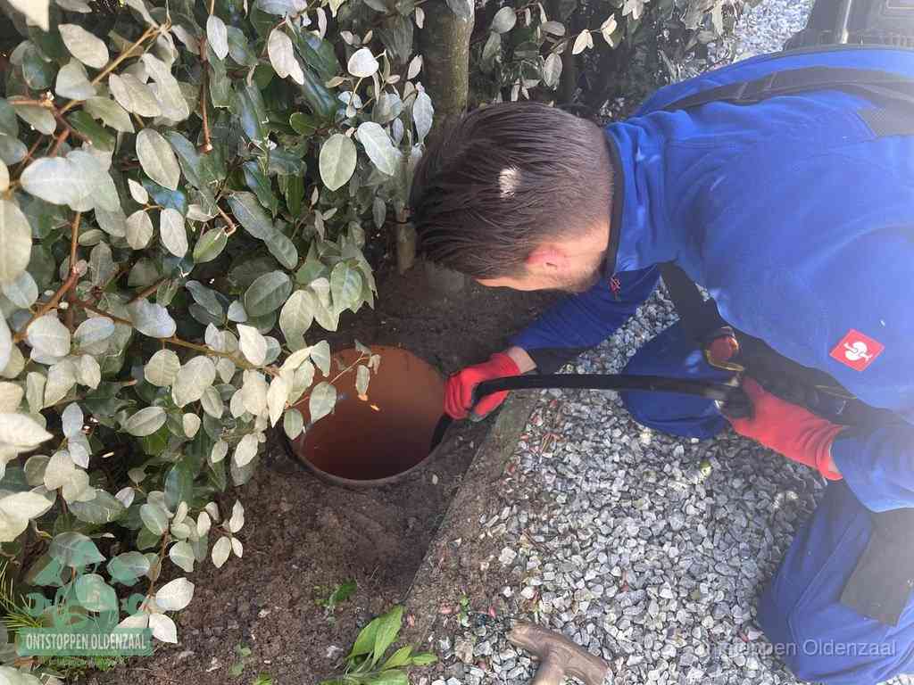 Een monteur voert een slang in een geopende rioolput in de tuin om het hoofdriool te ontstoppen in Oldenzaal