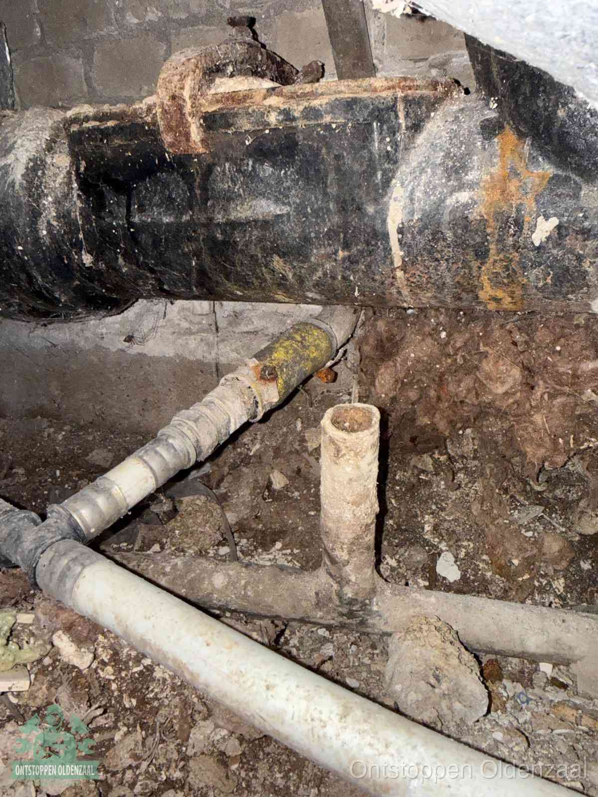 Een oude hoofdrioolbuis met roest- en kalkaanslag in een kruipruimte, oorzaak van terugkerende structurele rioolproblemen in Oldenzaal